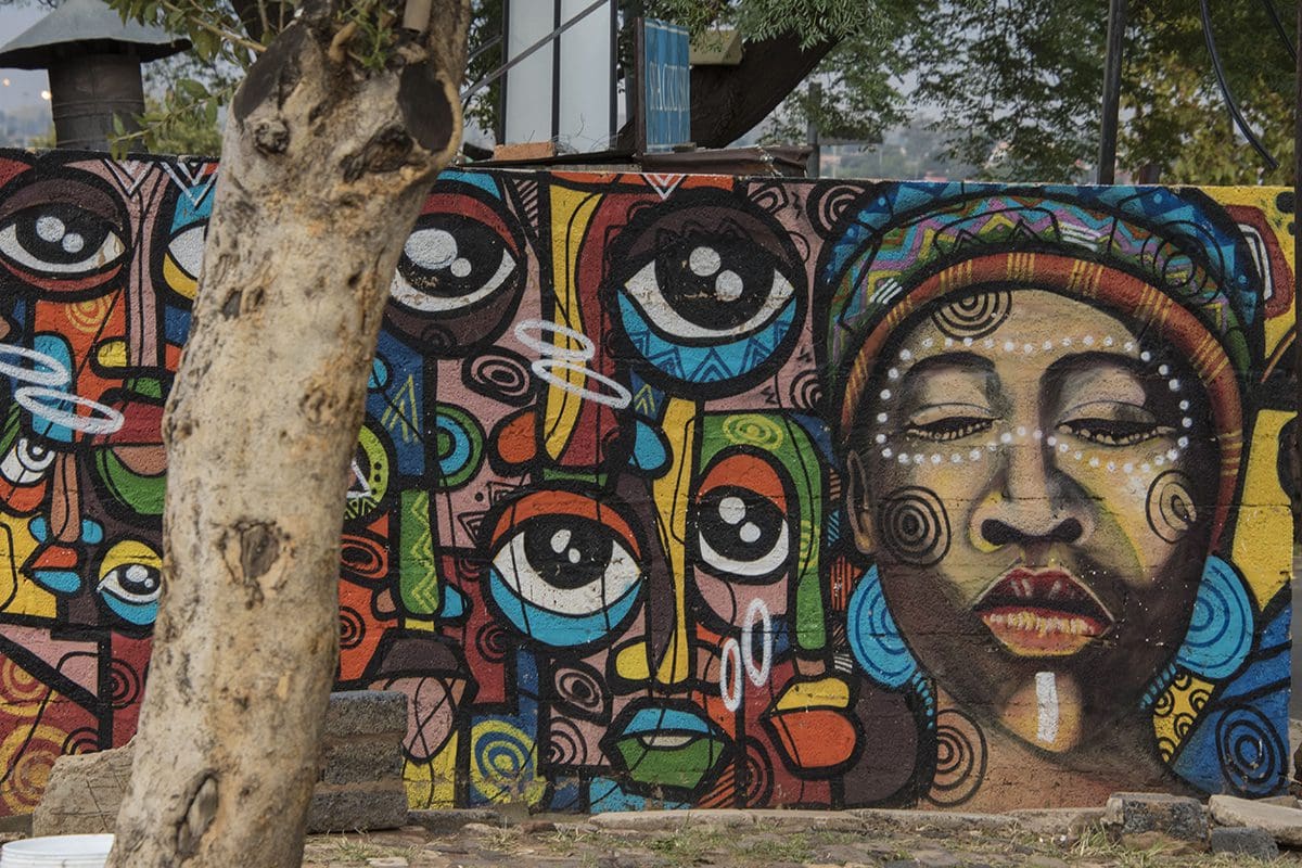 A colorful mural on a wall near a tree.