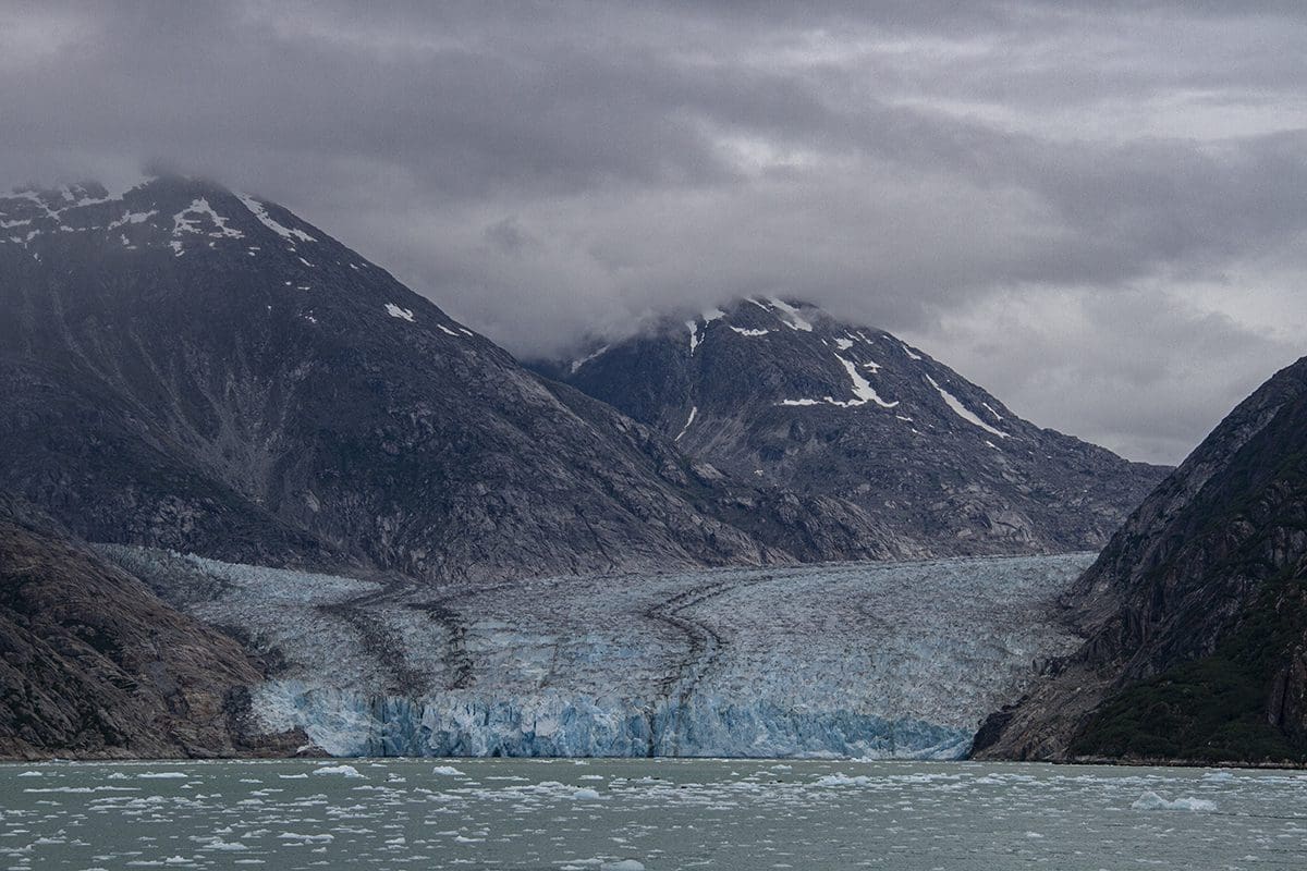 A glacier in a body of water under a cloudy sky.
