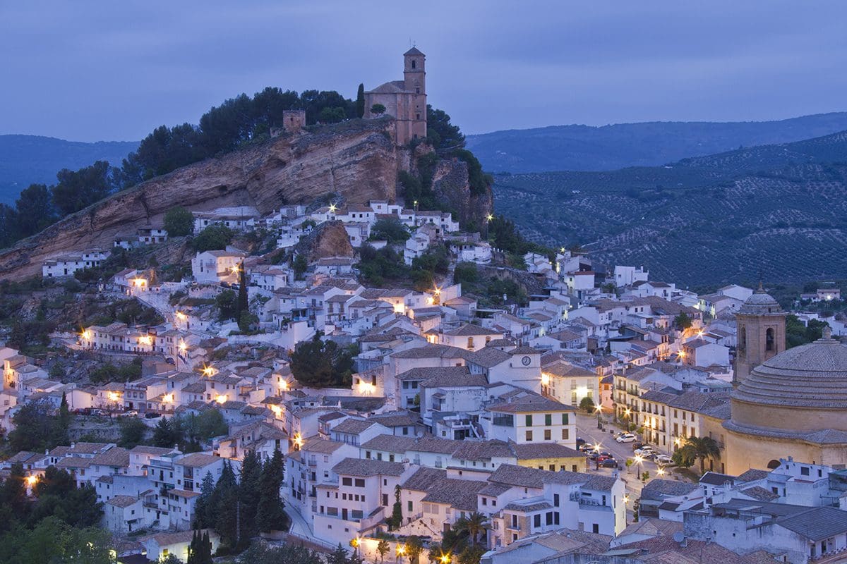 A town is lit up at night on top of a mountain.