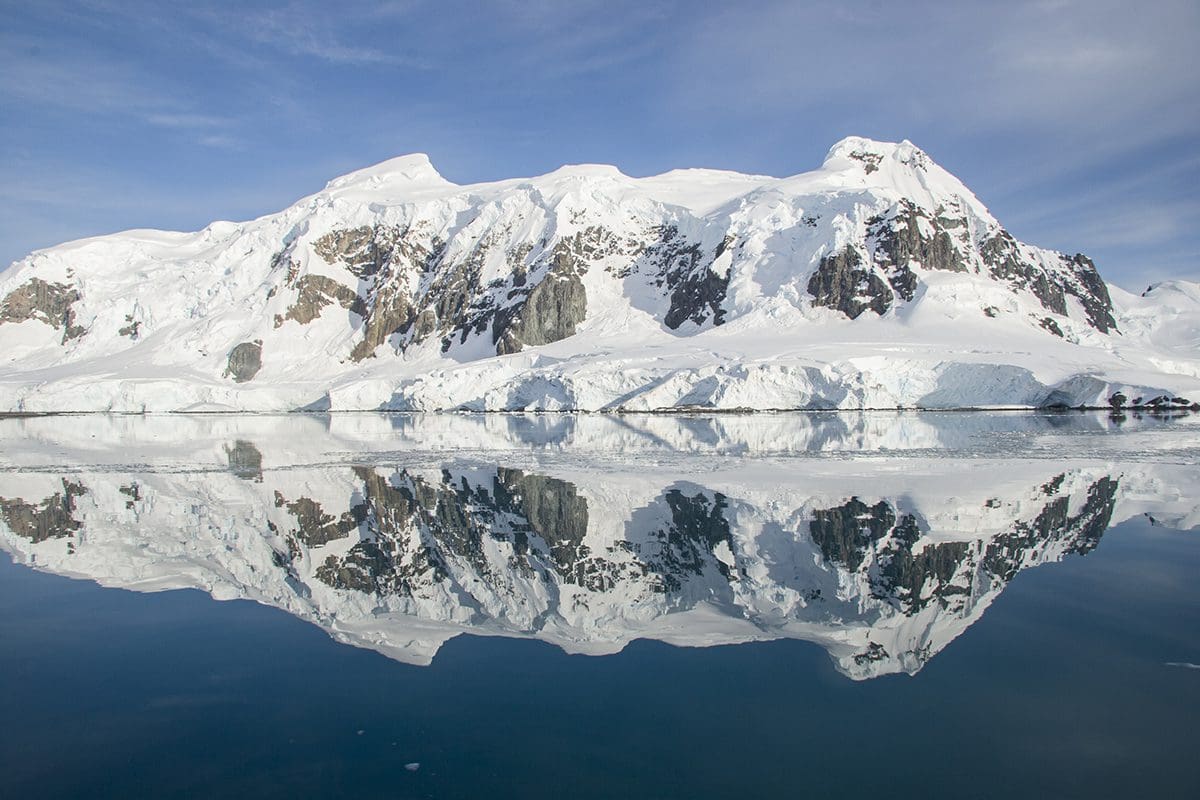 A snow covered mountain is reflected in a body of water.
