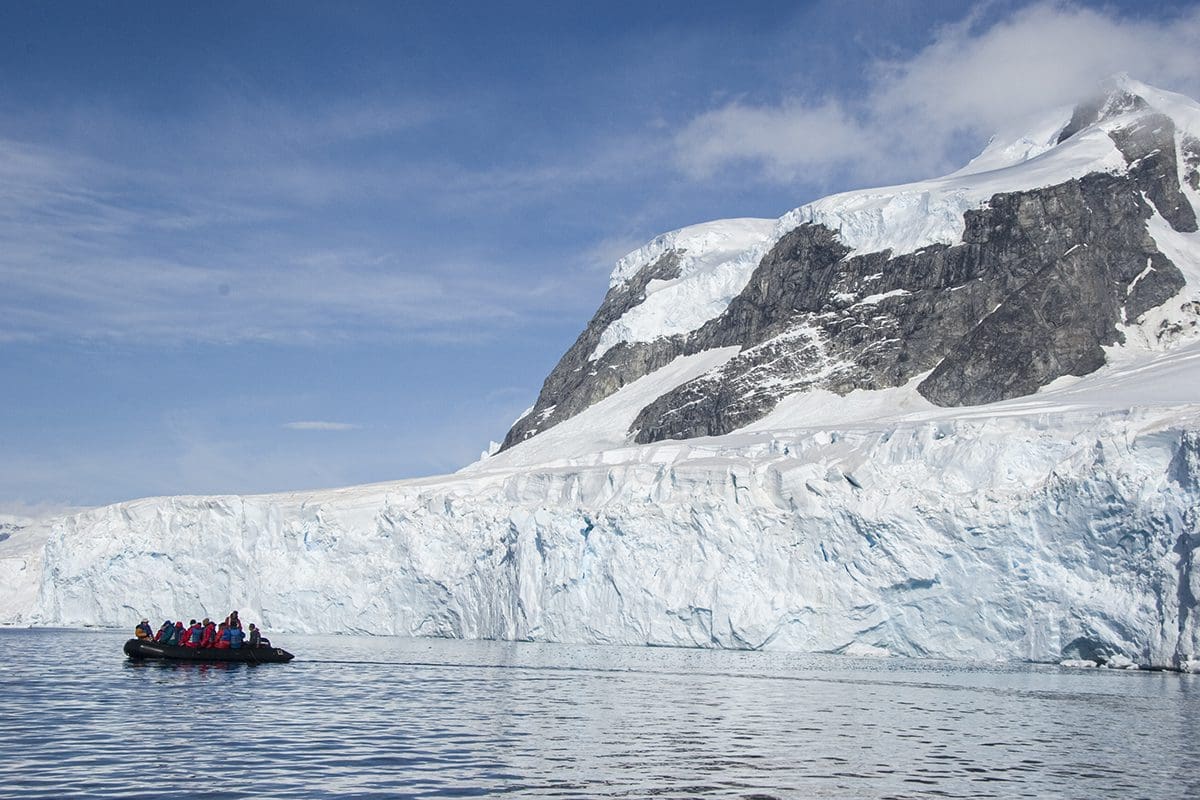 A group of people on a boat in front of an iceberg.