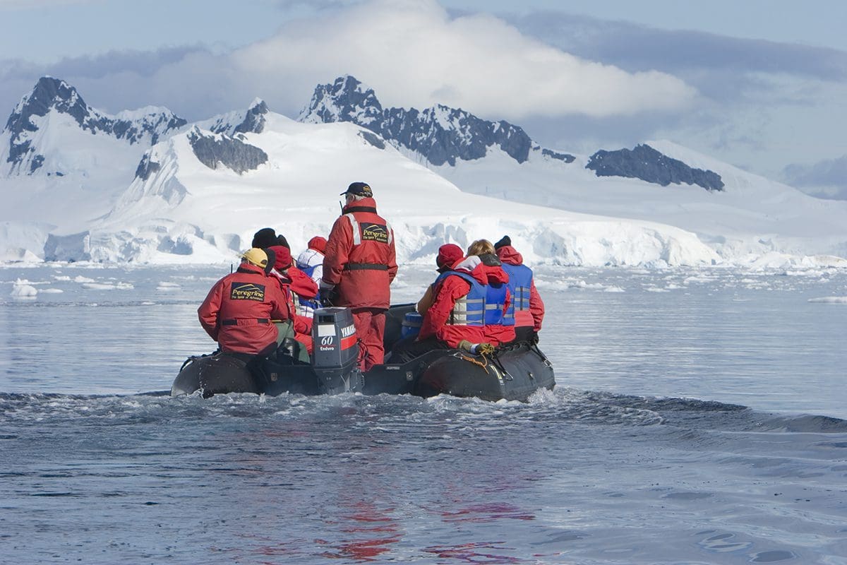 A group of people on a raft in the water near an iceberg.