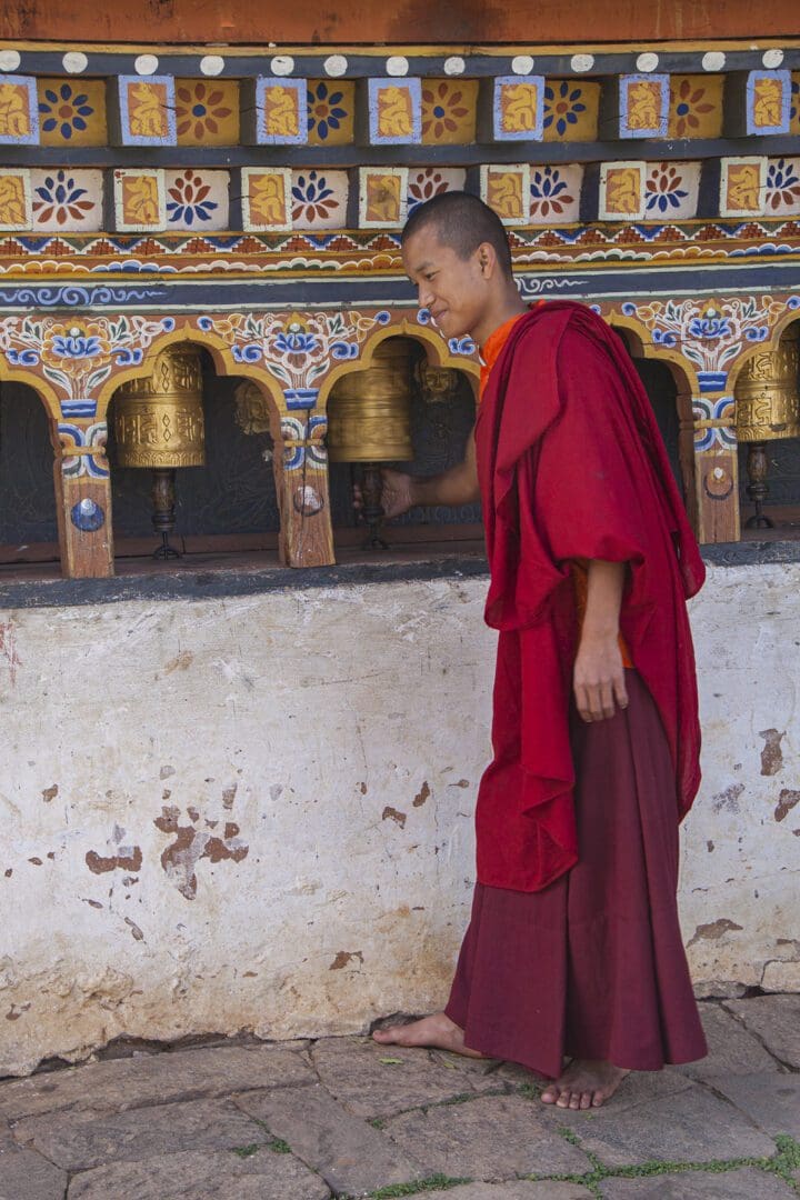 A monk in a red robe standing next to a set of bells.