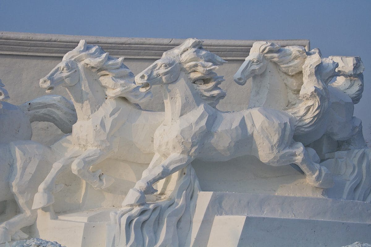 A white sculpture of horses on the side of a building.