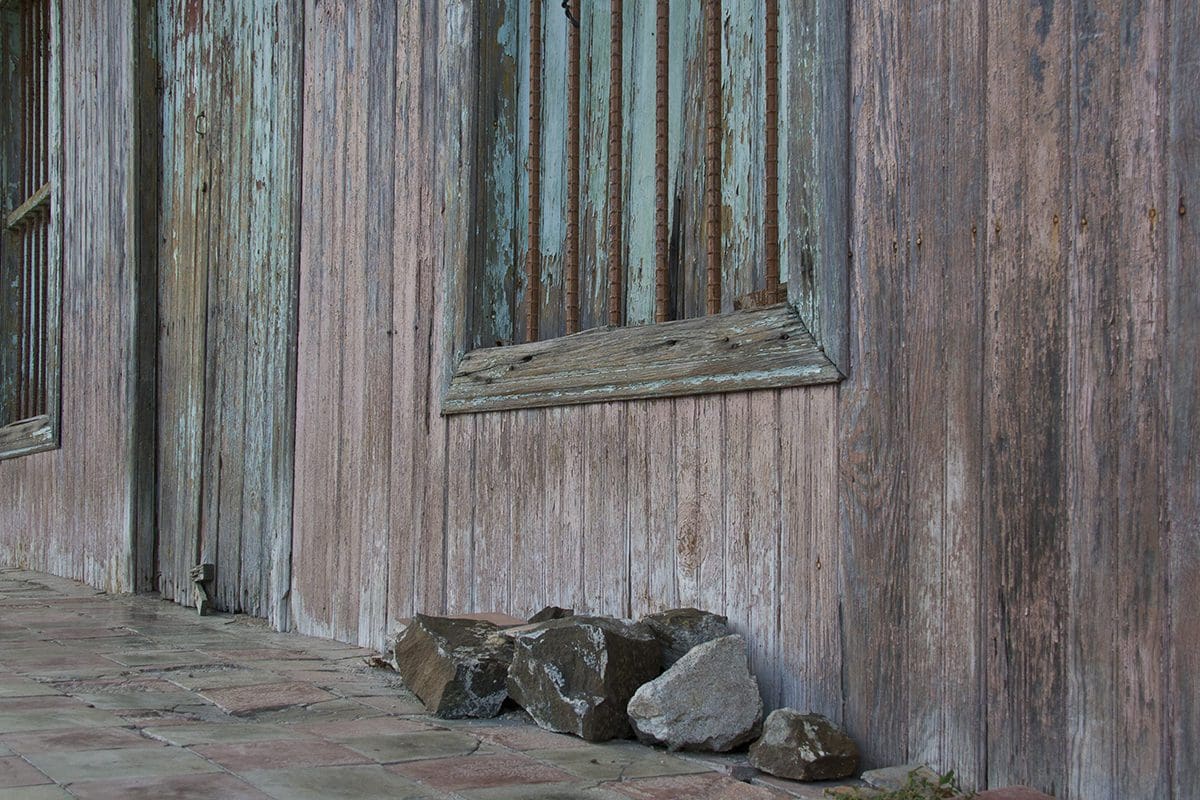 A wooden building with rusty windows and rocks on the ground.