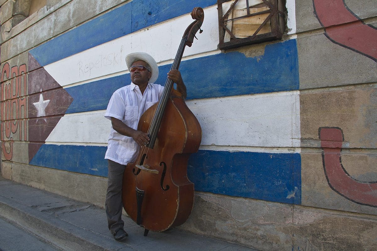 A man holding a cello in front of a wall.