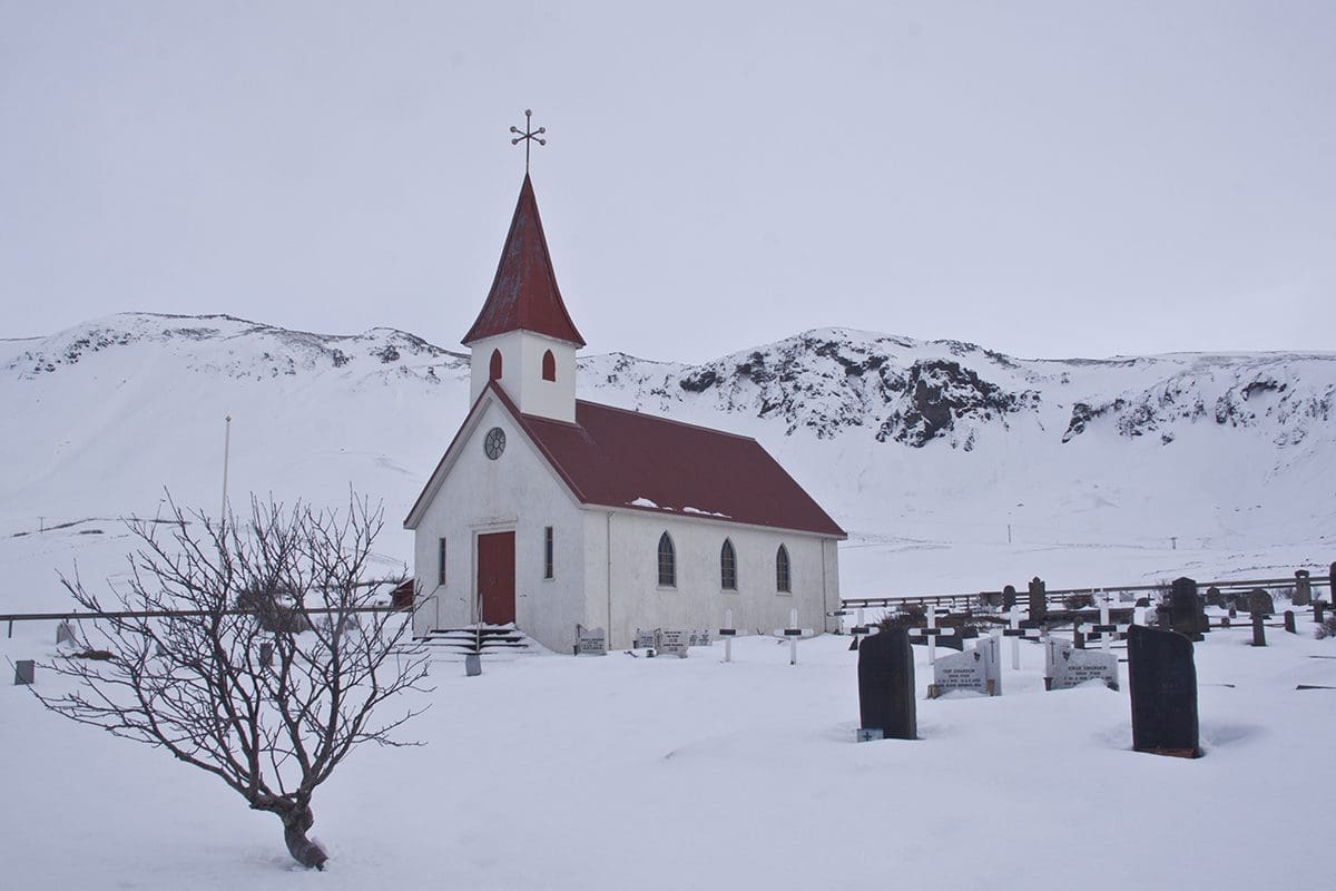 A small white church with a steeple in the snow.