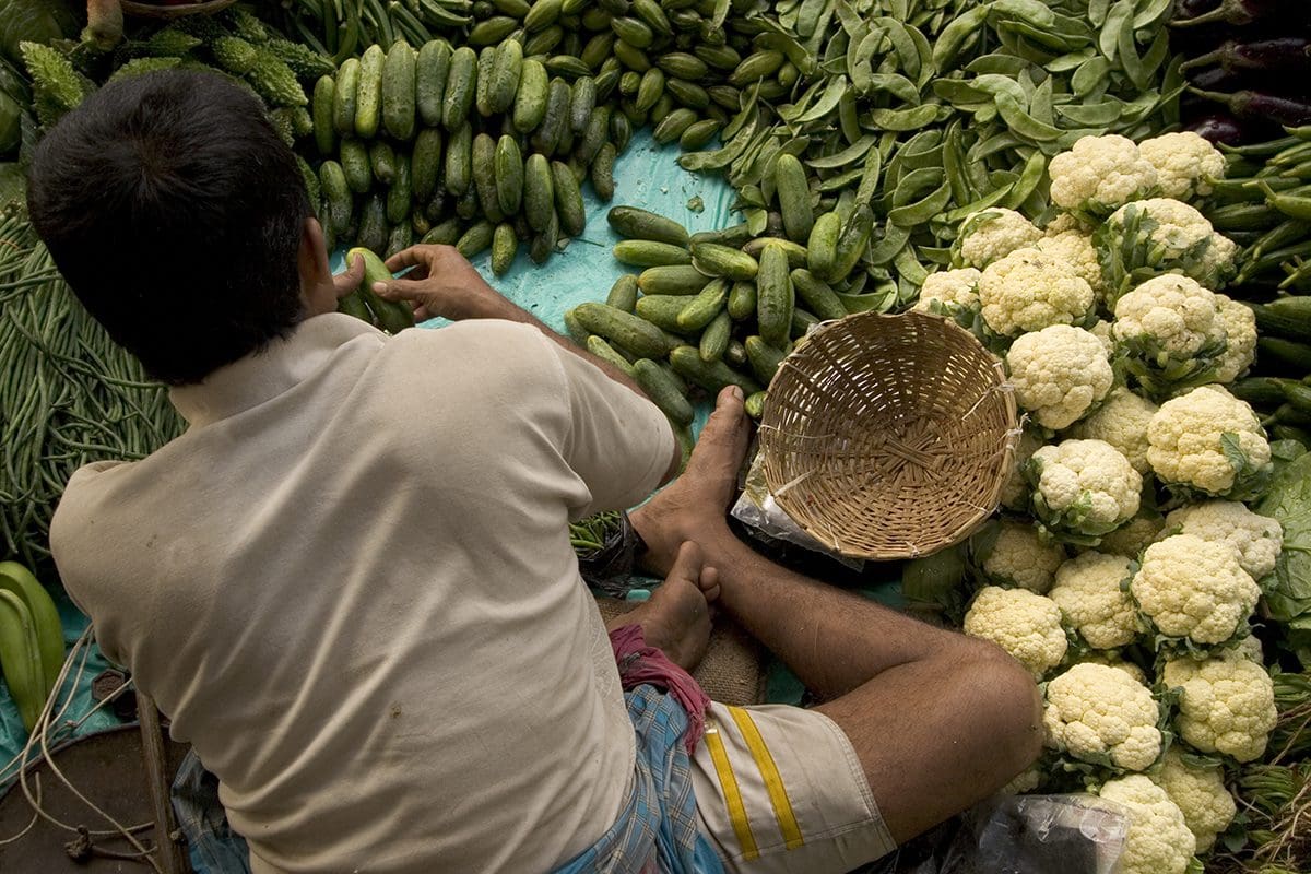 A man sits on the ground next to a bunch of vegetables.