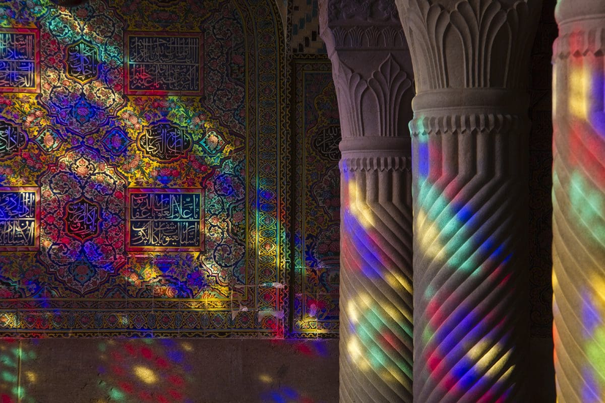 A colorful light shines through pillars in an islamic building.