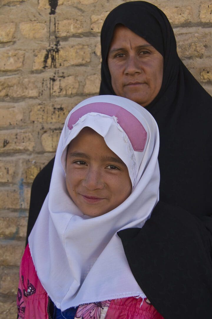 A young girl in a hijab poses for a photo with her mother.