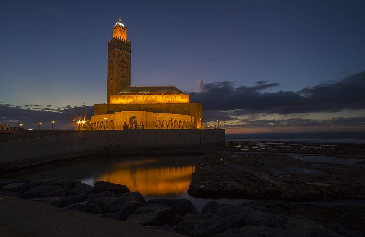 A mosque is lit up at night near the ocean.