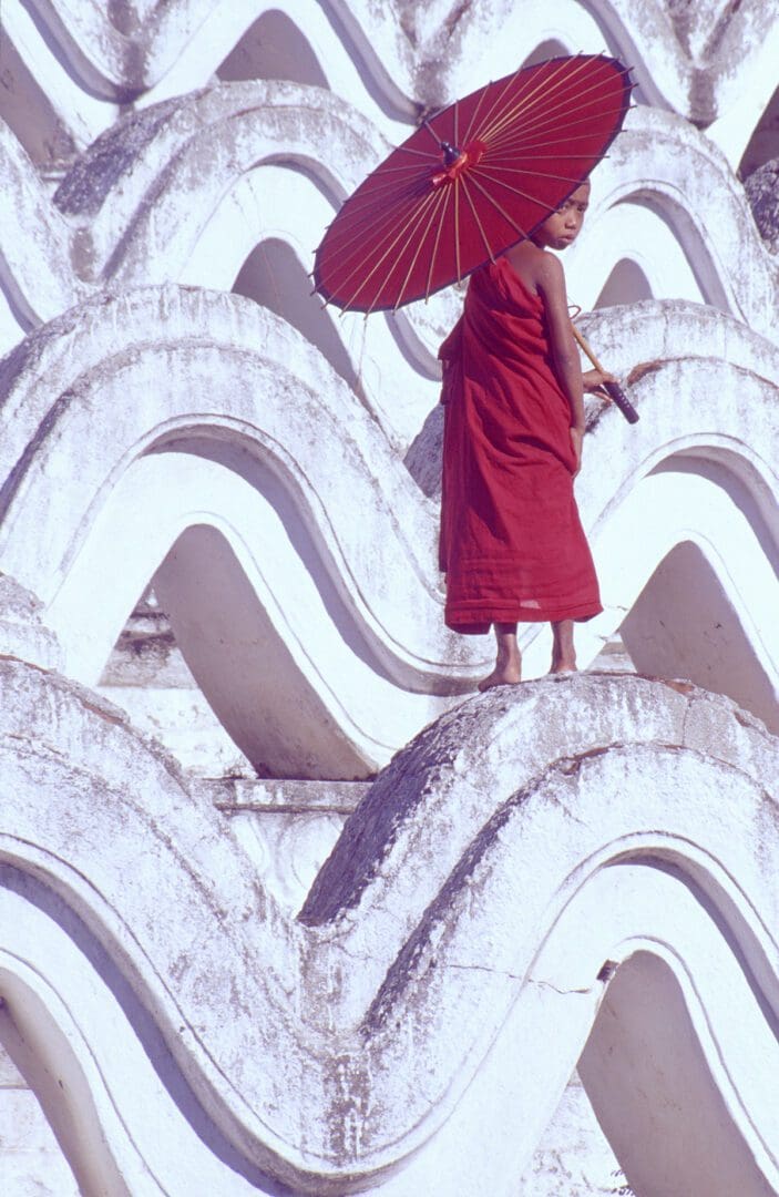 A young monk holding a red umbrella.