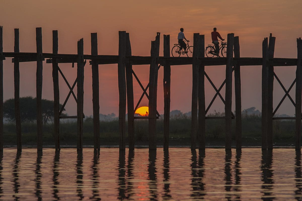 Two people riding bikes on a wooden bridge at sunset.