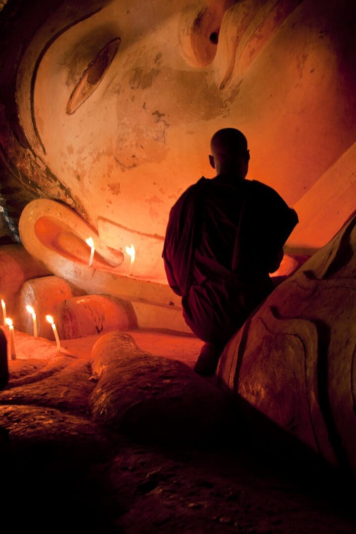 A buddhist monk sits in front of a large buddha statue.