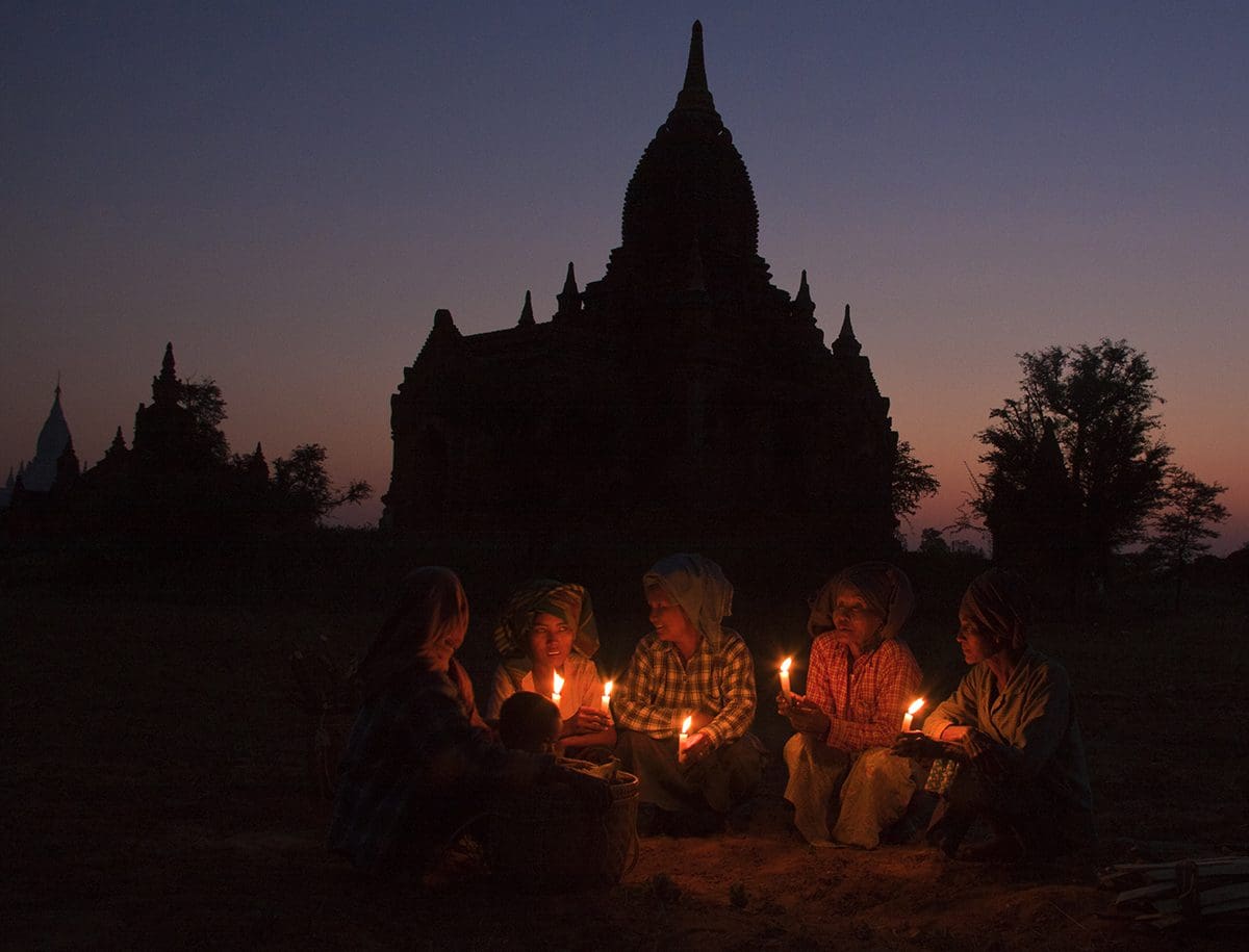 A group of people sitting around a temple at dusk.