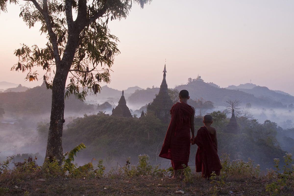 Two monks standing on a hill overlooking a temple.