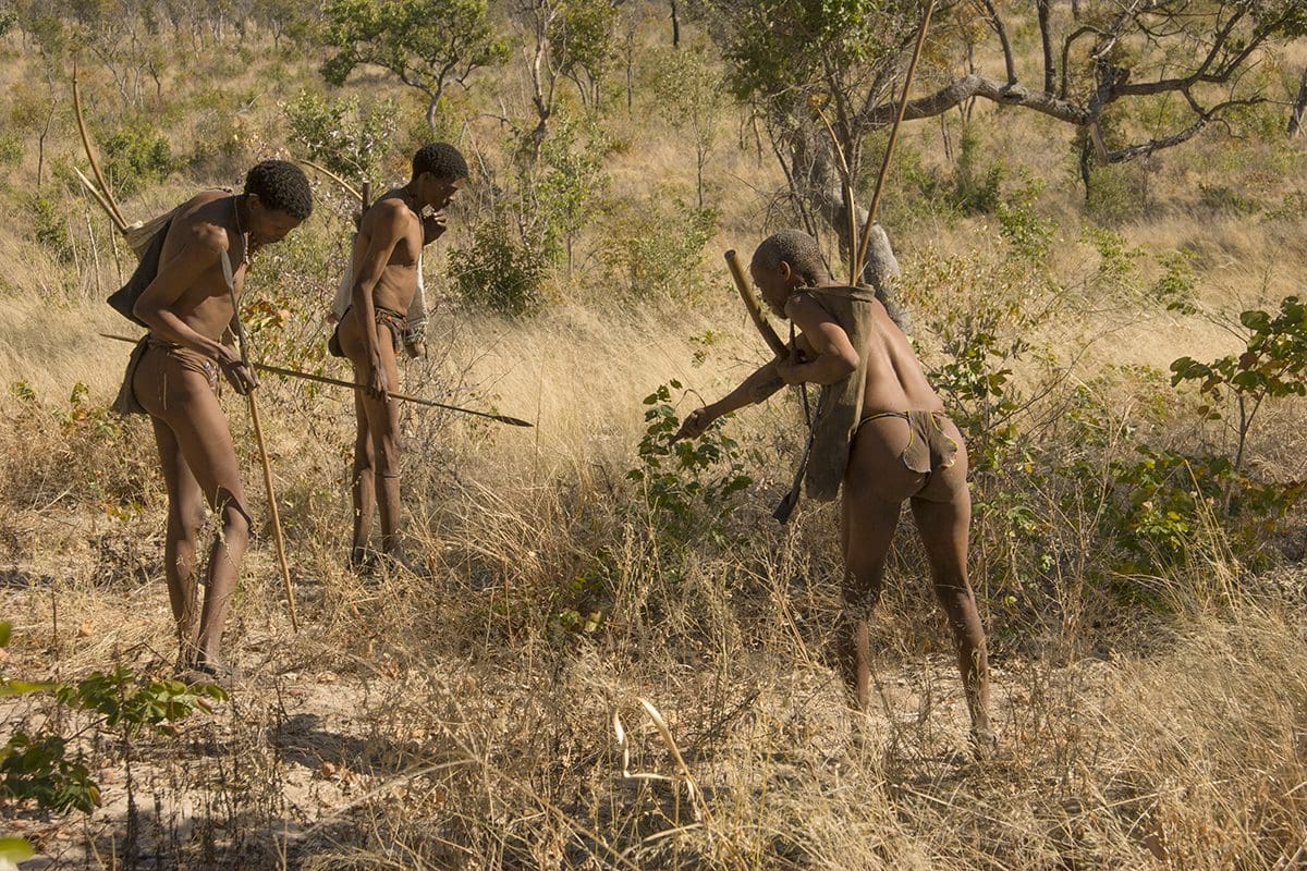 Three naked men standing in a field with sticks.