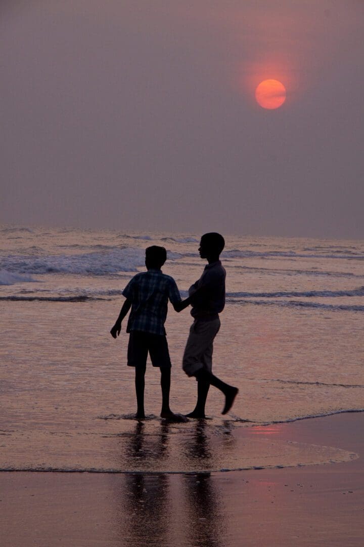 Two boys walking on the beach at sunset.