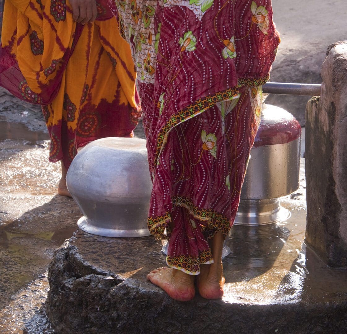 Two women standing next to a water well.