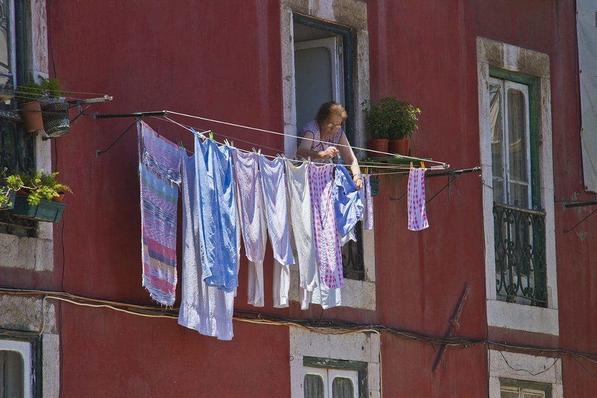 A girl is hanging clothes on a line outside of a red building.