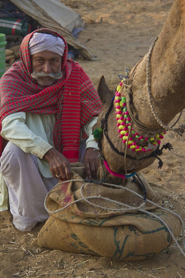 A man sitting next to a camel.
