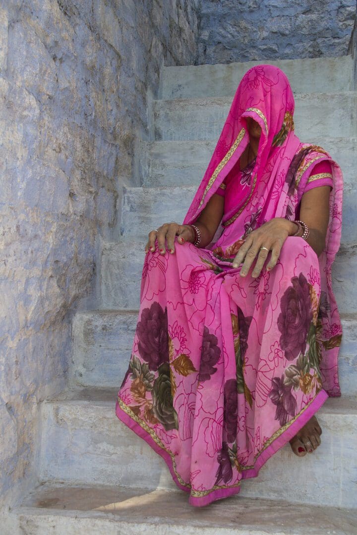 A woman in a pink sari sitting on steps.