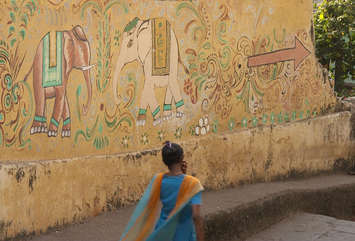 A girl walking down a street with a painted wall.