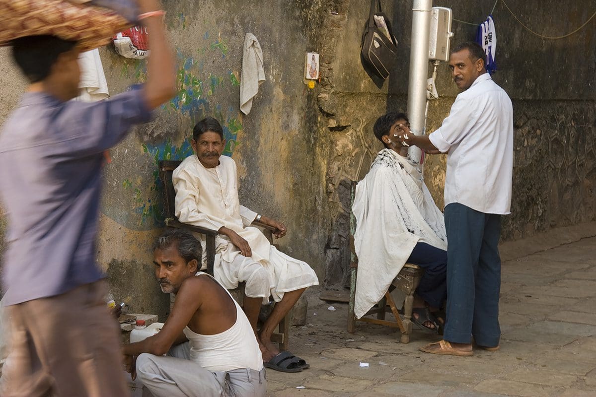 A barber cutting a man's hair on a street.