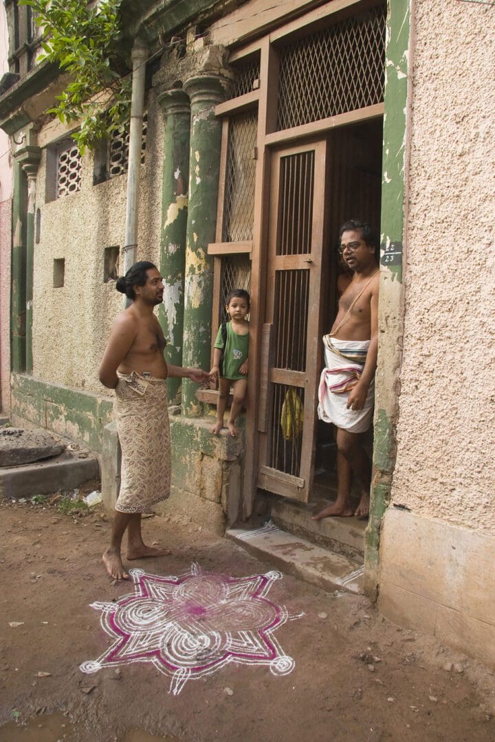 A group of people standing in front of a house with a rangoli.