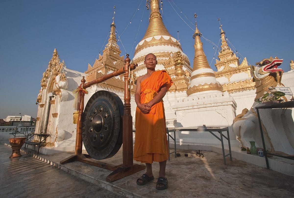 A monk standing in front of a large golden pagoda.