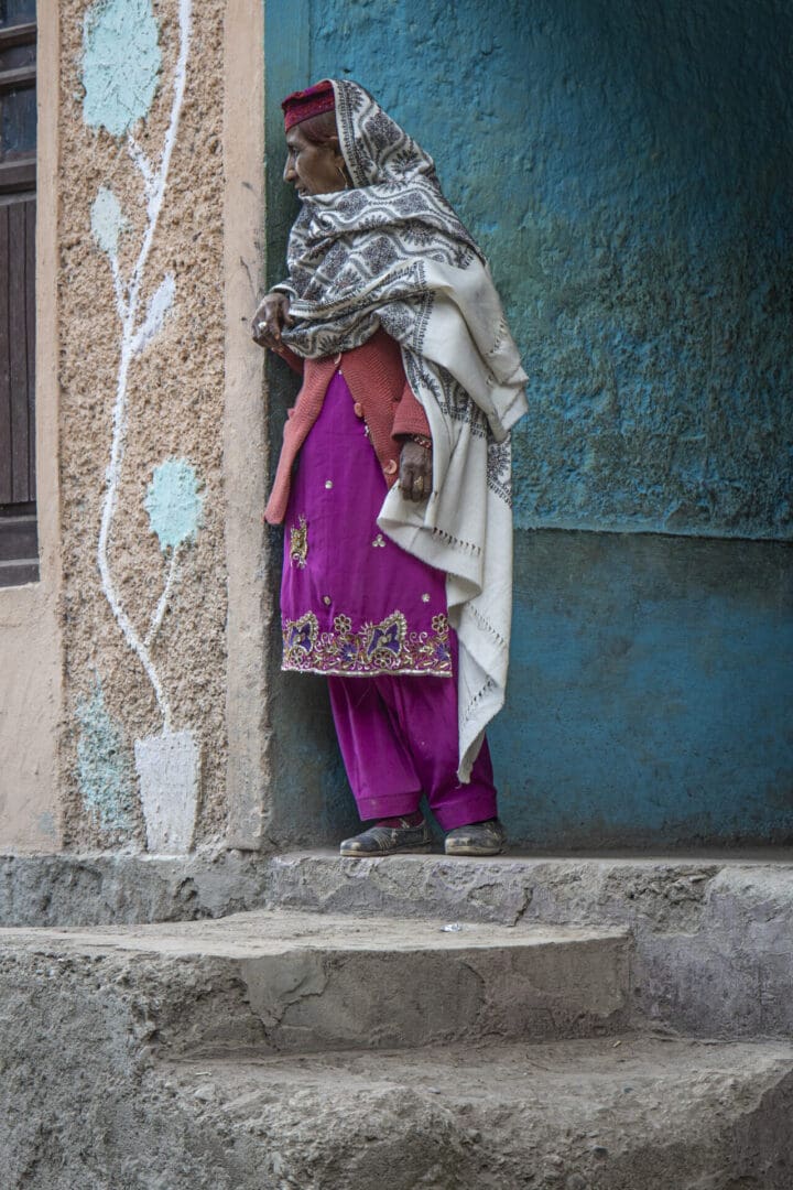 A woman wearing a shawl is standing on the steps of a building.