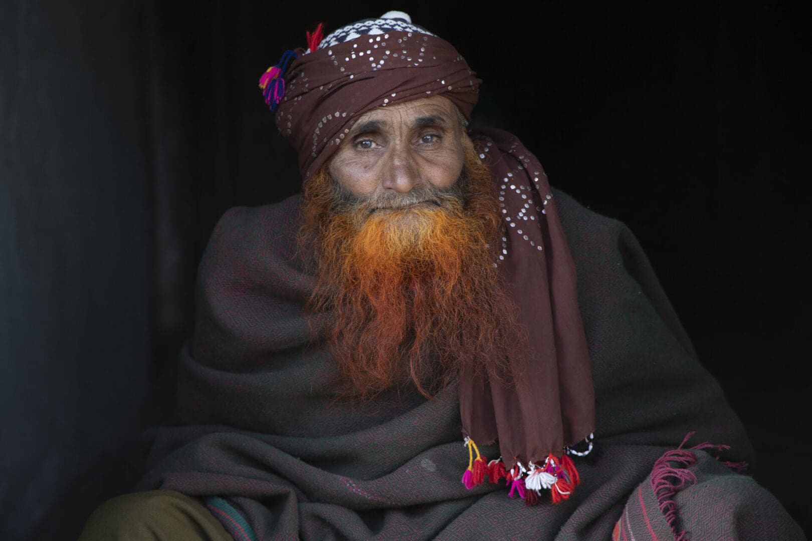 An old man with a red beard sitting in a dark room.