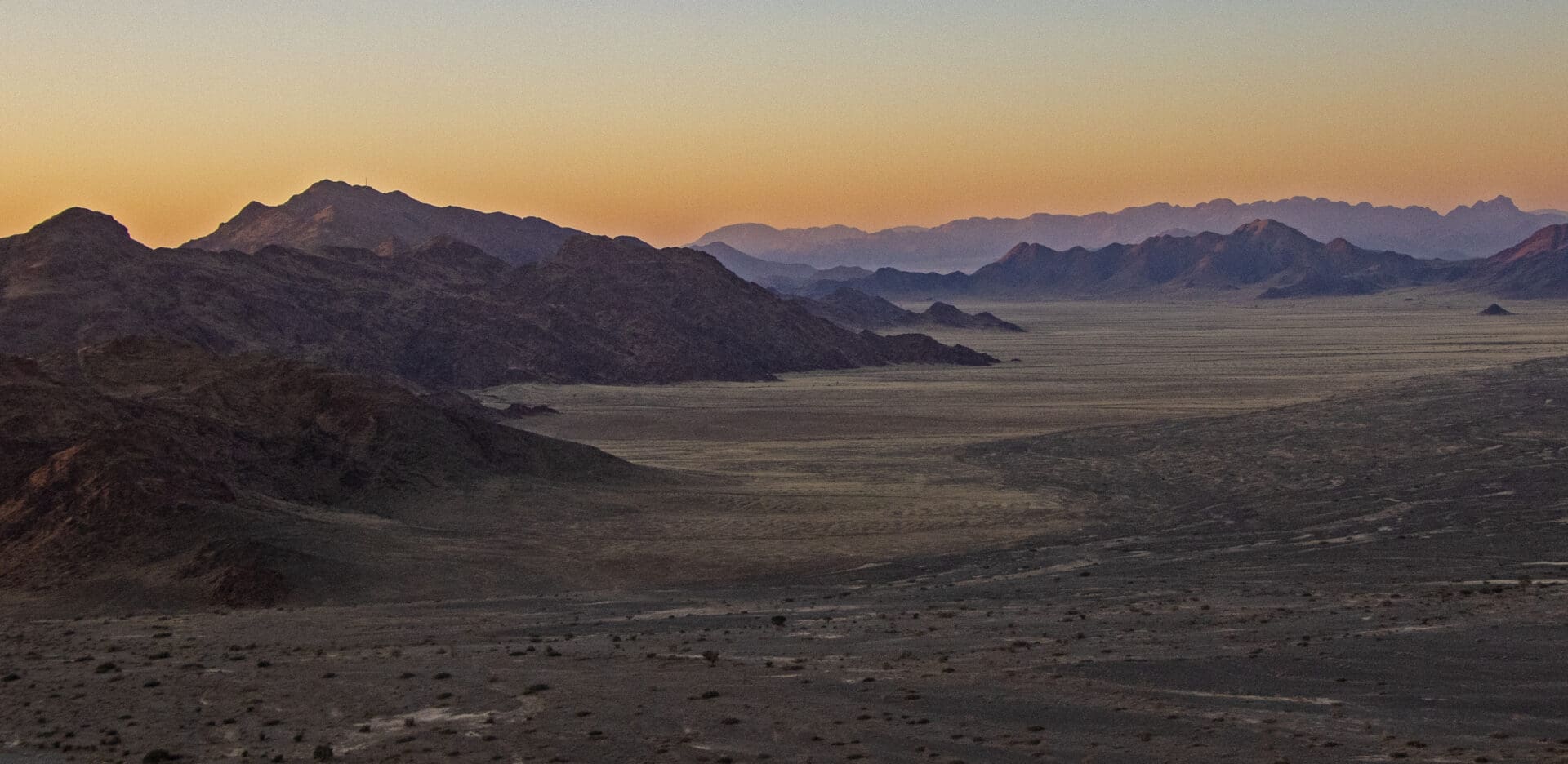 A desert landscape at sunset with mountains in the background.