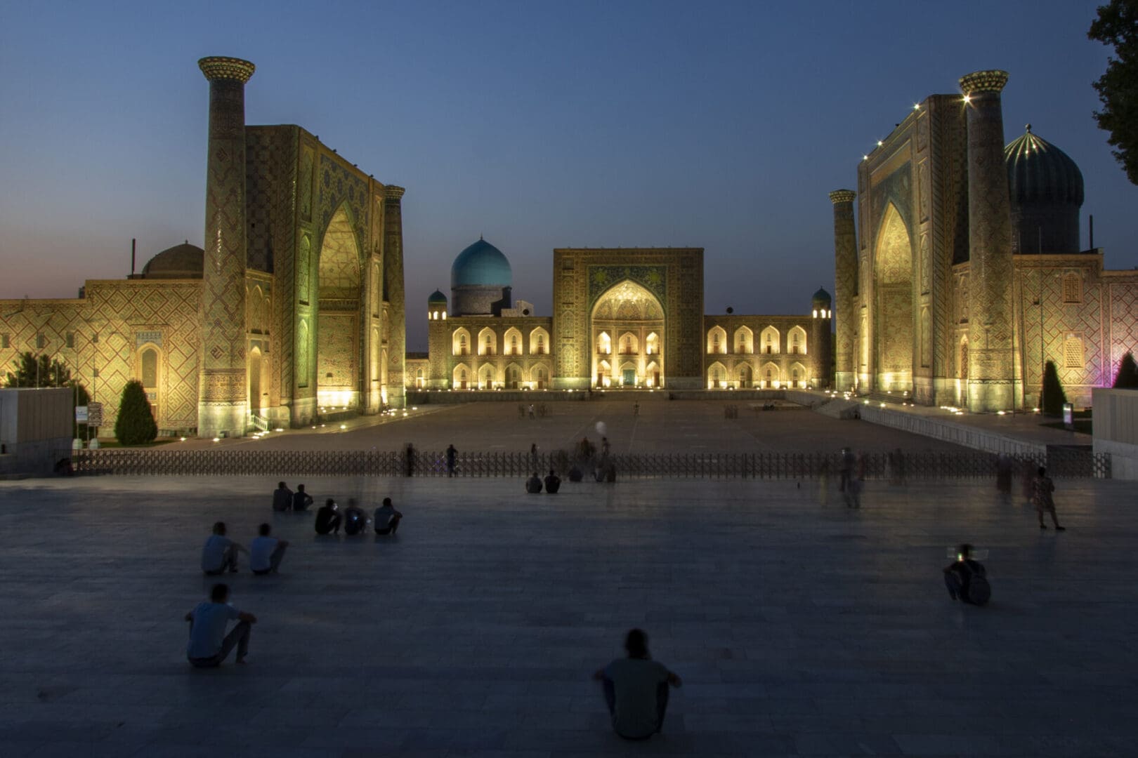 People are sitting in the courtyard of a mosque at dusk.